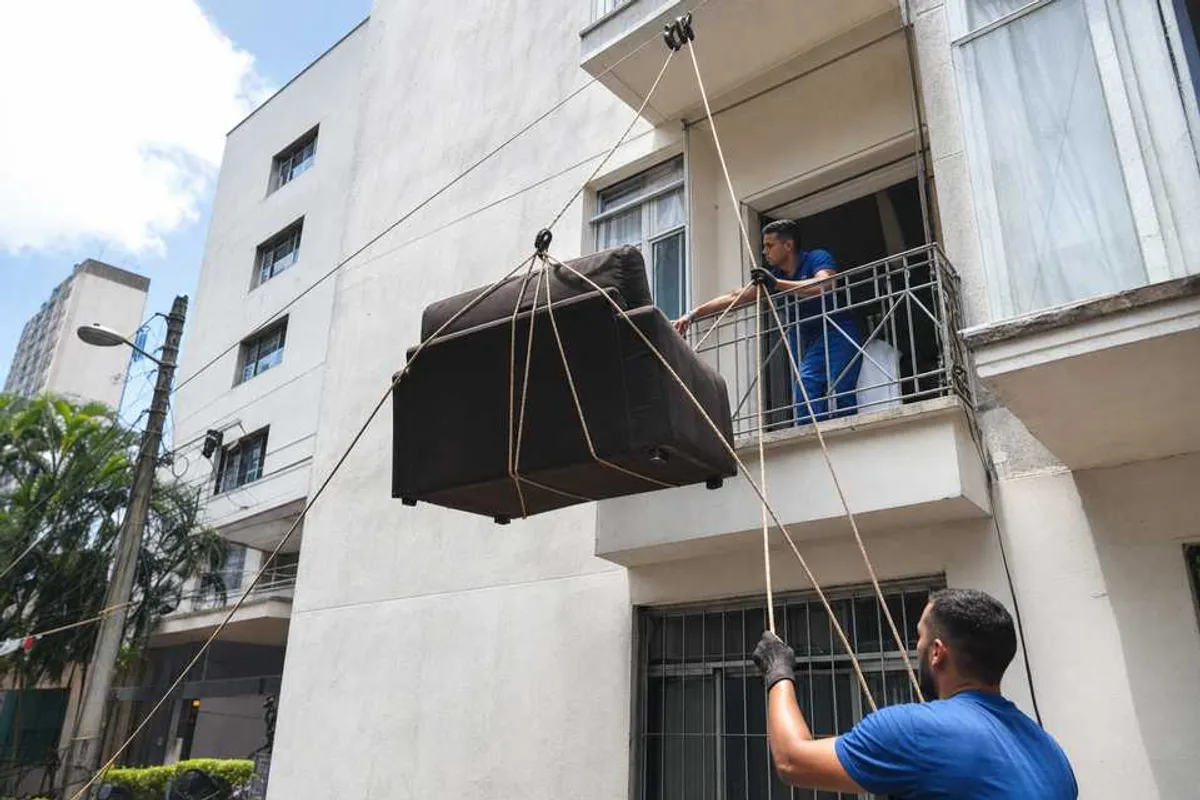 Profissionais içando um sofá pela janela de um apartamento com cordas e roldanas durante uma mudança em Dourados